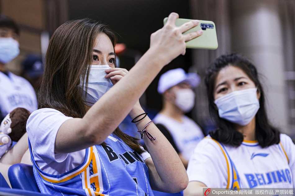 一位戴着口罩的美女粉丝依然难掩激动之情，她手举手机记录赛场瞬间，背景中可以看到其他粉丝高高举起“书豪”的名字牌。