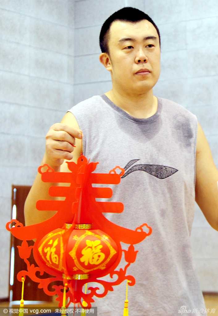 主教练郭士强被弟子们簇拥在中间，他手里拿着红色的吉祥物，神情温和地看着镜头，仿佛一位大家长正带着孩子们准备过年。
