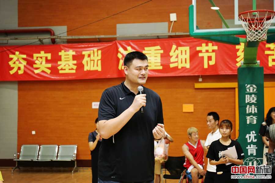 姚明侧身亲自指导邓亚萍投篮姿势，邓亚萍神情专注地托着篮球准备出手，两人身后是正在热身的残疾人运动员，画面里满是跨界的友爱与专注